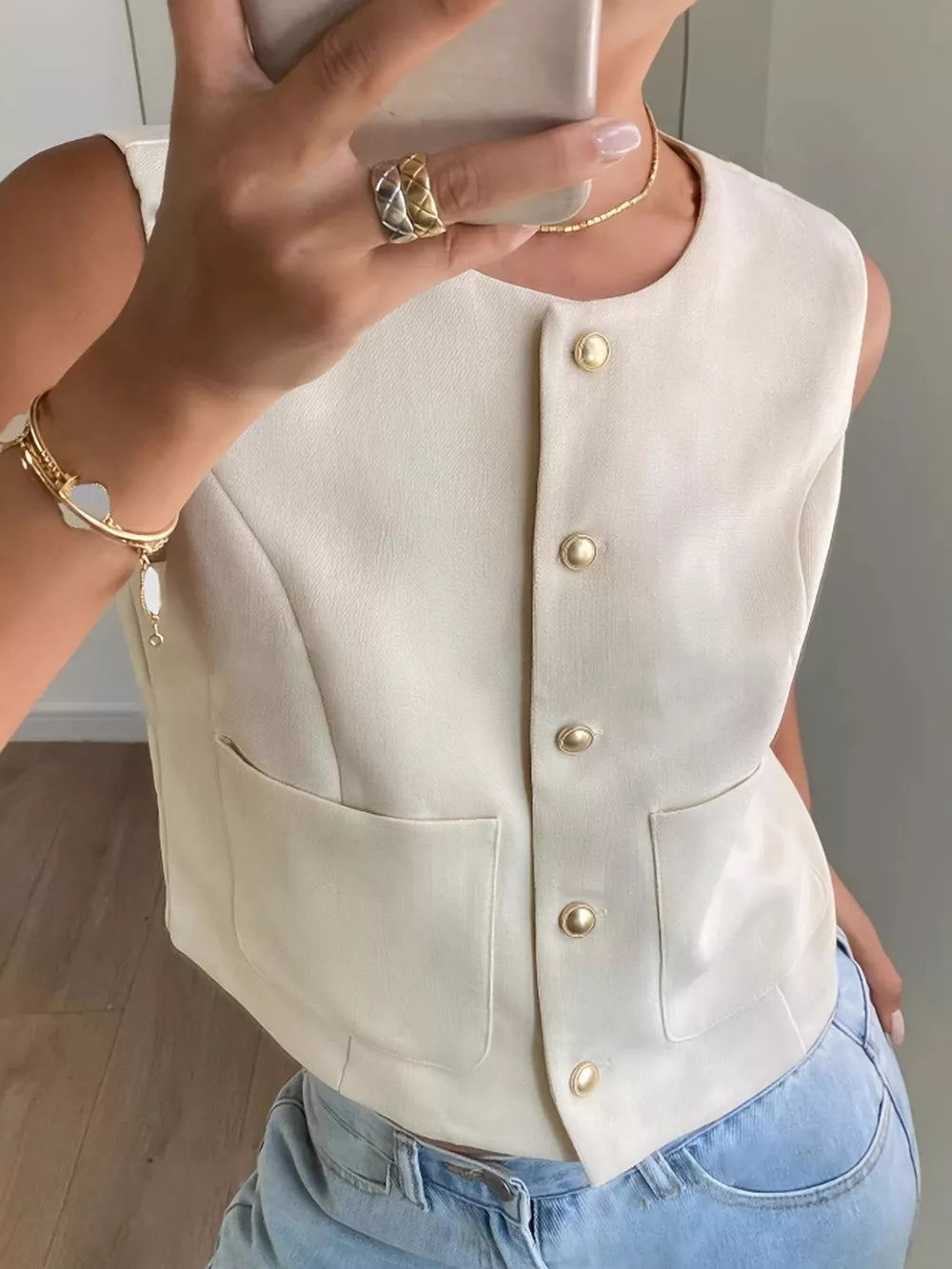 Cream button-down sleeveless vest with crew neck and two front pockets.