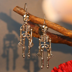 Gold skeleton silhouette drop earrings with detailed bones and articulated limbs.