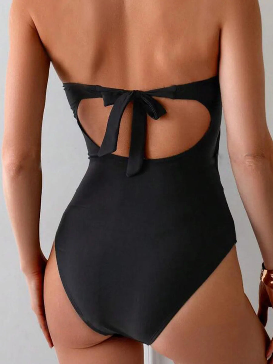 Black one-piece swimsuit with strapless neckline, cutout back, and bow detail