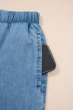 Maternity wide-leg chambray jeans in light blue denim with an elastic waistband and a phone in the pocket.