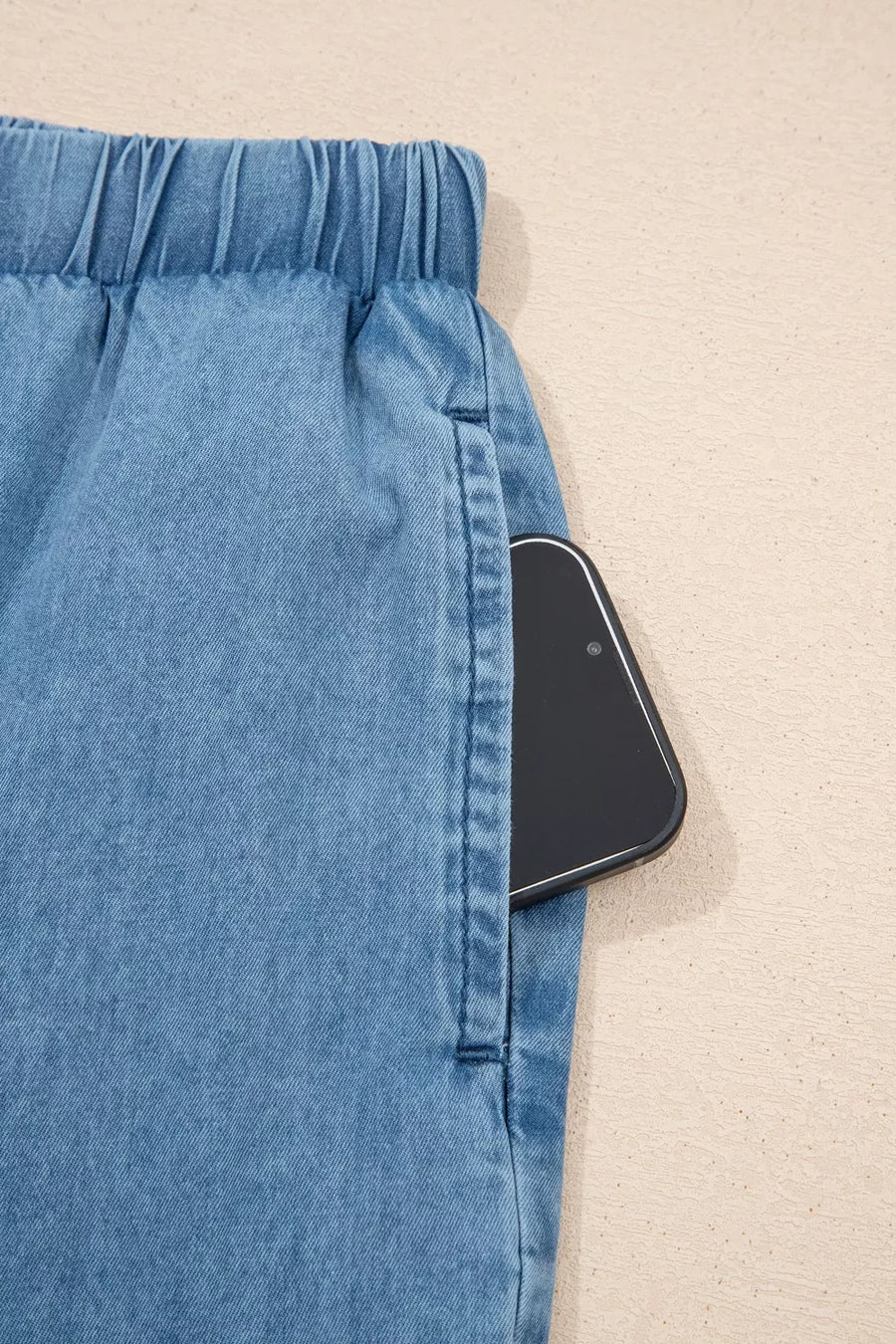 Maternity wide-leg chambray jeans in light blue denim with an elastic waistband and a phone in the pocket.