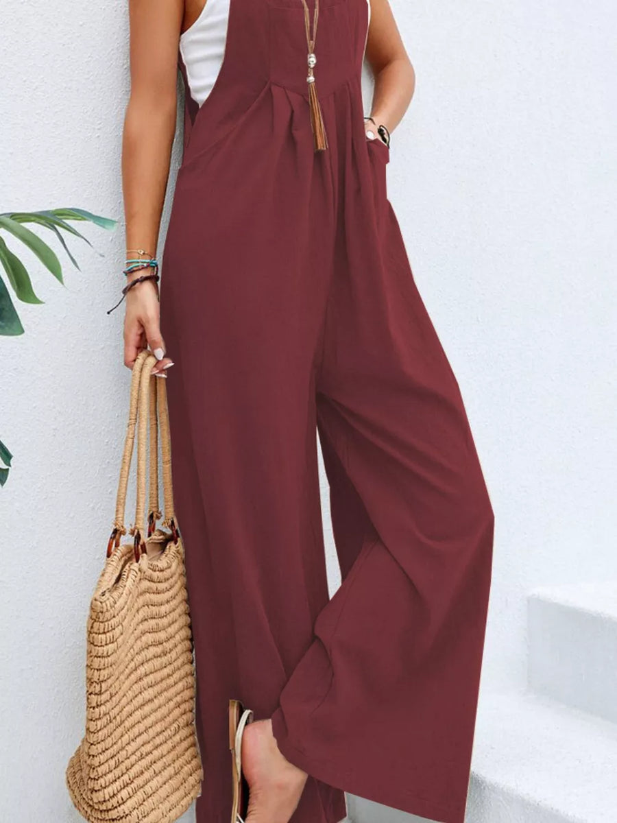 Burgundy wide-leg romper with pockets, adjustable straps, and a tassel necklace.