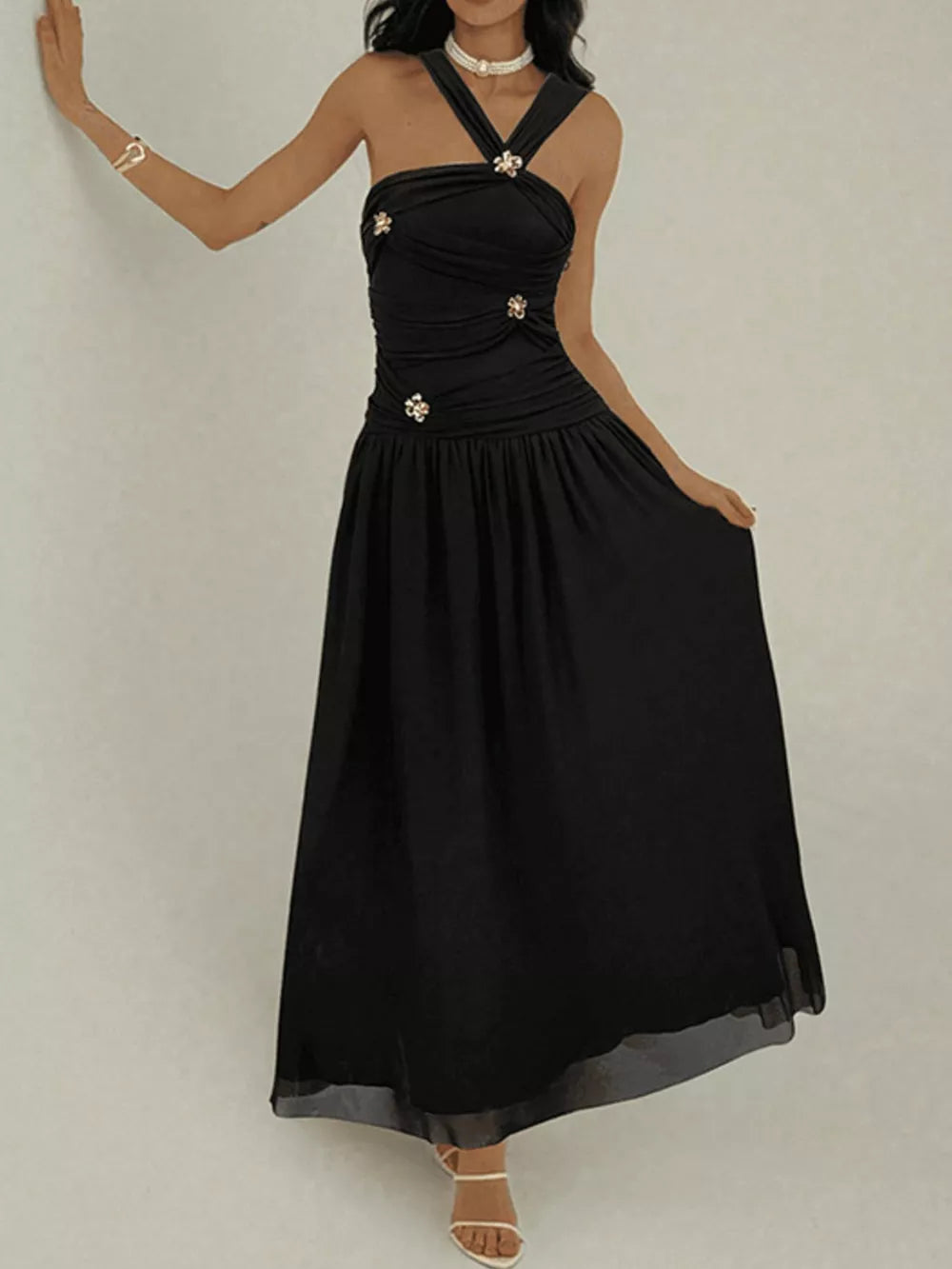 Black ruched sleeveless maxi dress with embellishments and a halter neckline.