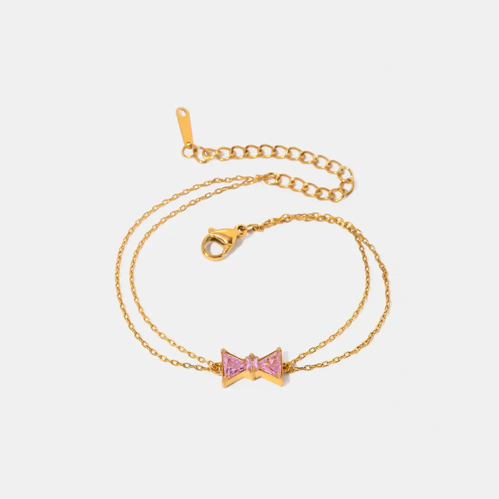 Gold chain bracelet with a pink gemstone bow charm
