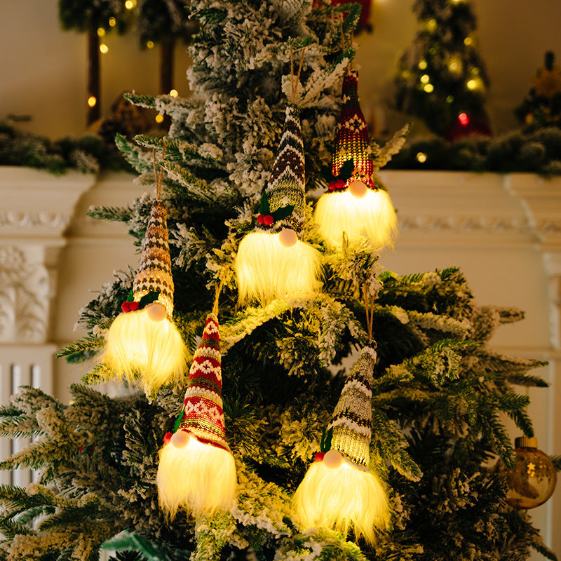 Illuminated gnome ornaments with knitted hats and fluffy white beards hang on a Christmas tree.