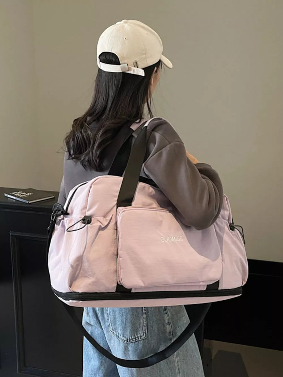 Light purple duffle bag with black trim and exterior pockets, worn over the shoulder.