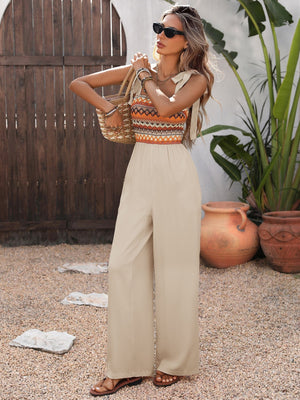 Smocked tie shoulder romper in beige with patterned bodice and wide legs.