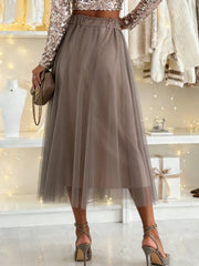 Sheer mesh A-line midi skirt in taupe with elastic waistband, styled with heels.