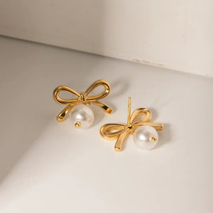 Gold bow pearl drop earrings with a small gold bead detail.