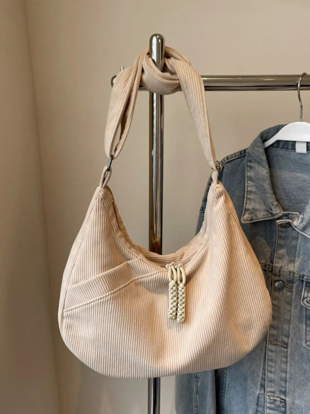 Beige corduroy crescent shoulder bag with braided tassels and front pocket