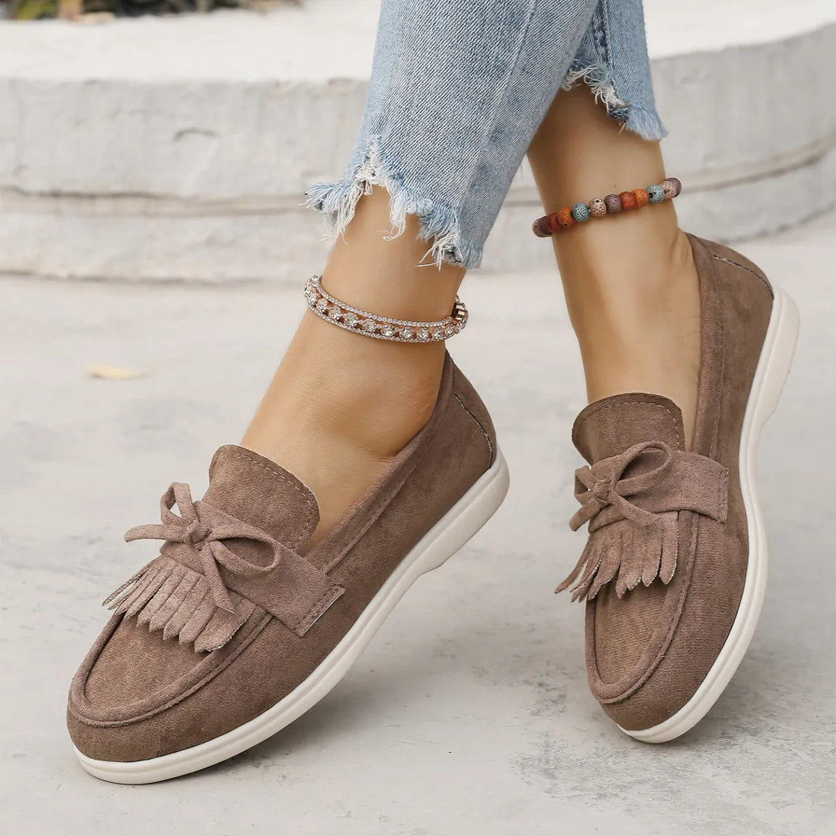 Fringe bow loafer flats in taupe suede with a white sole.