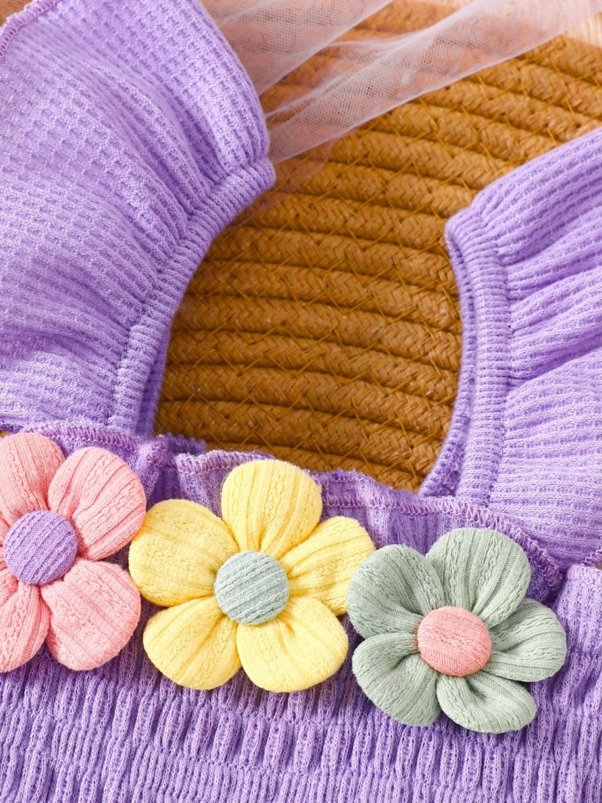 Purple smocked jumpsuit with floral appliques in pink, yellow, and pastel blue.