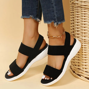 Black knit strap sandals with white soles and a gold ankle chain.
