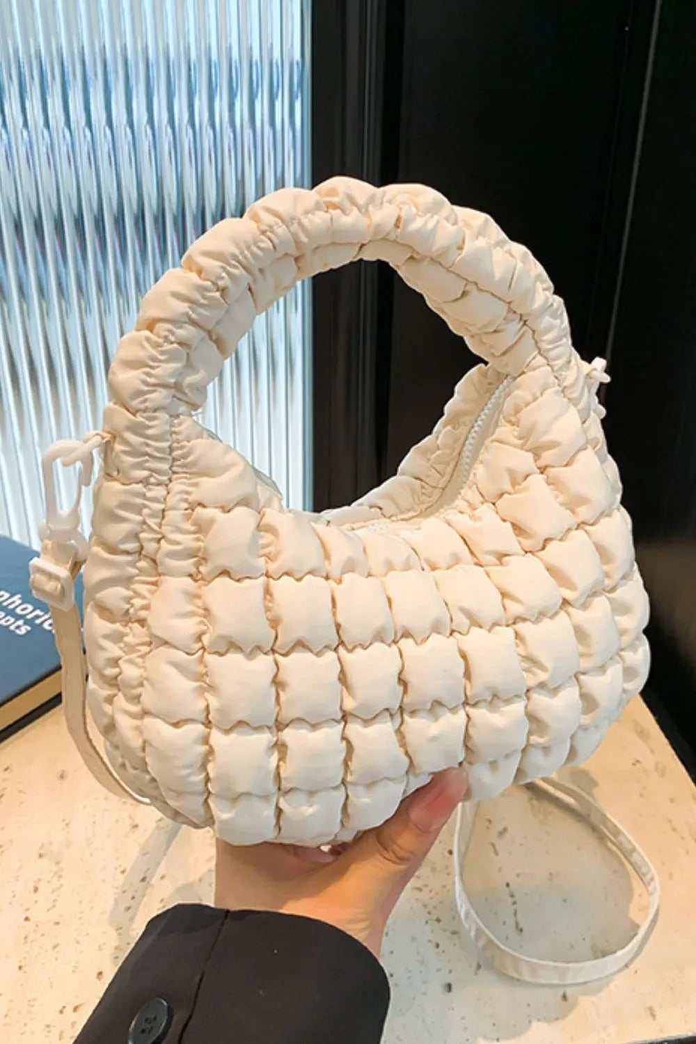 Padded crescent crossbody bag in ivory with sculptural texture and ruched handle.