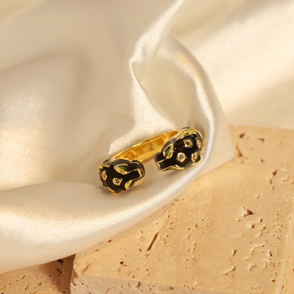 Gold open ring with black enamel panther heads and green gem eyes