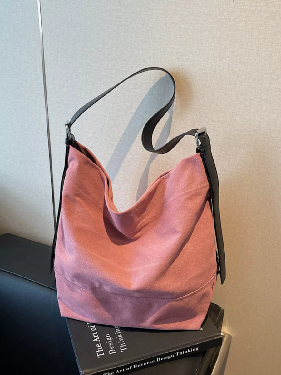 Pink hobo bag with adjustable black straps and a suede-like finish.