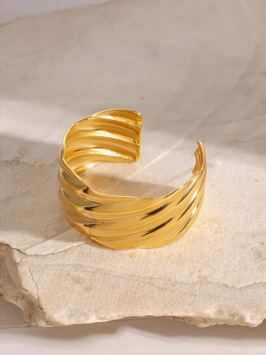 Gold cuff bracelet with sculpted wave detail, 18K gold-plated and adjustable.