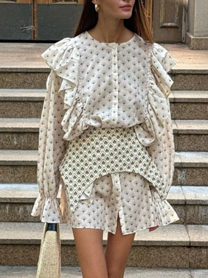 Cream printed blouse with ruffled sleeves and a matching mini skirt, styled with a patterned overlay.