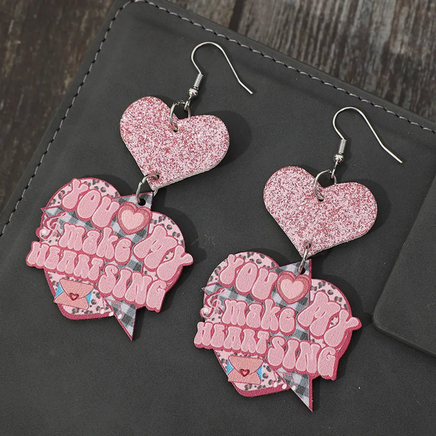 Blush pink glittered heart earrings with "You Make My Heart Sing" text detail