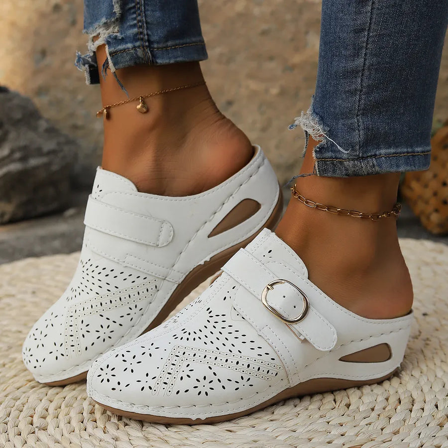 White laser-cut buckle mule wedges with perforated floral patterns and adjustable strap.