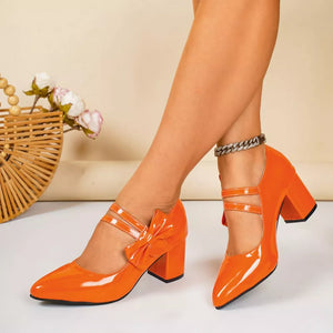 Orange patent leather pumps with pointed toe, block heel, and bow detail.