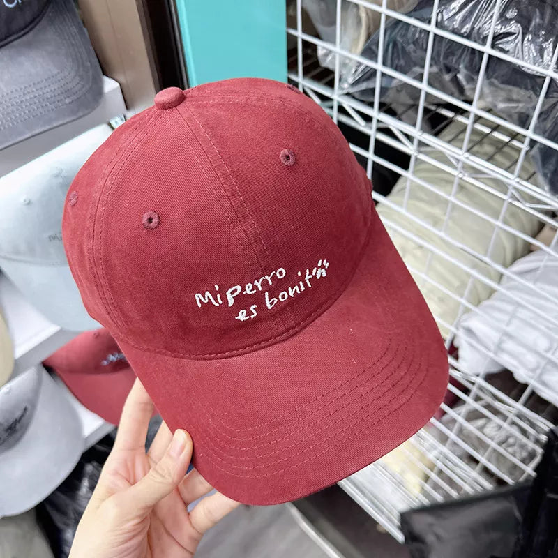 Red baseball cap with "Mi perro es bonit" embroidery and paw print detail.