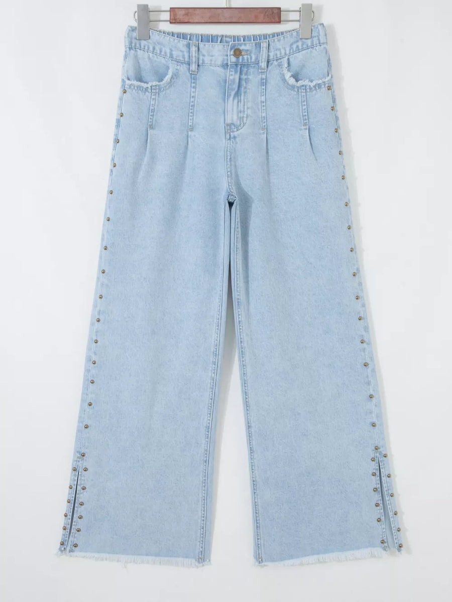 Light wash denim wide-leg jeans with studded side slits and frayed hem.
