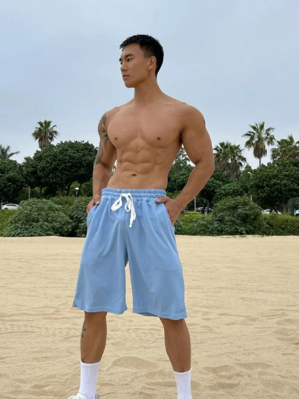 Light blue relaxed-fit drawstring bermuda shorts with pockets on a man at the beach.