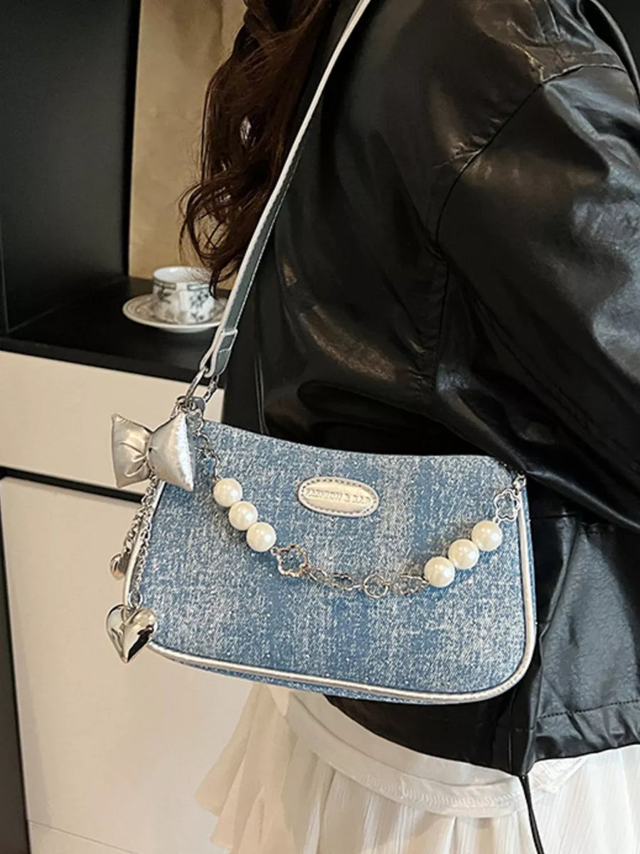 Light denim shoulder bag with pearl chain, heart charm, and bow detail.