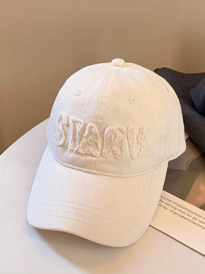 Milky white cotton baseball cap with distressed applique letters and a curved brim.
