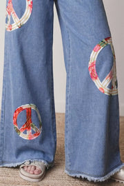 Light wash denim wide-leg jeans with floral peace sign appliqués and frayed hems.