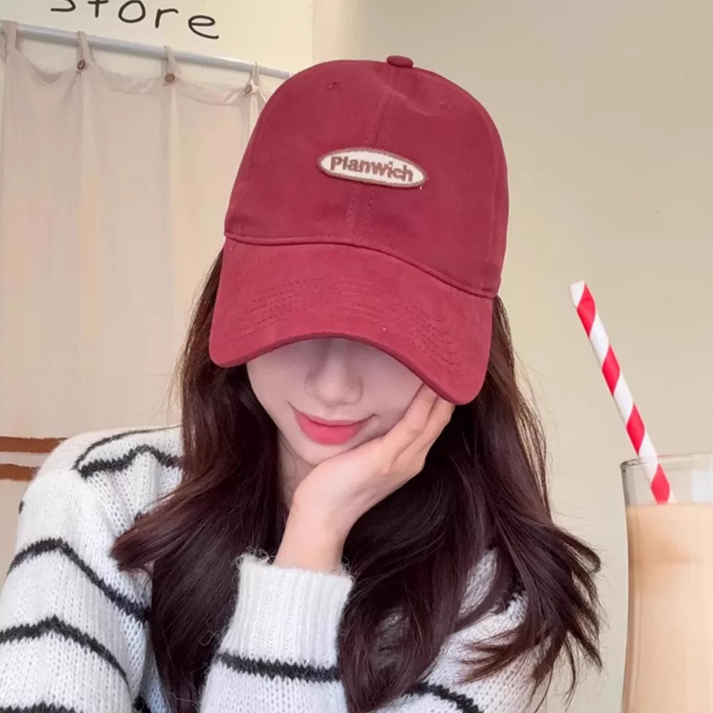 Maroon baseball cap with oval embroidered logo patch, styled with a striped sweater.