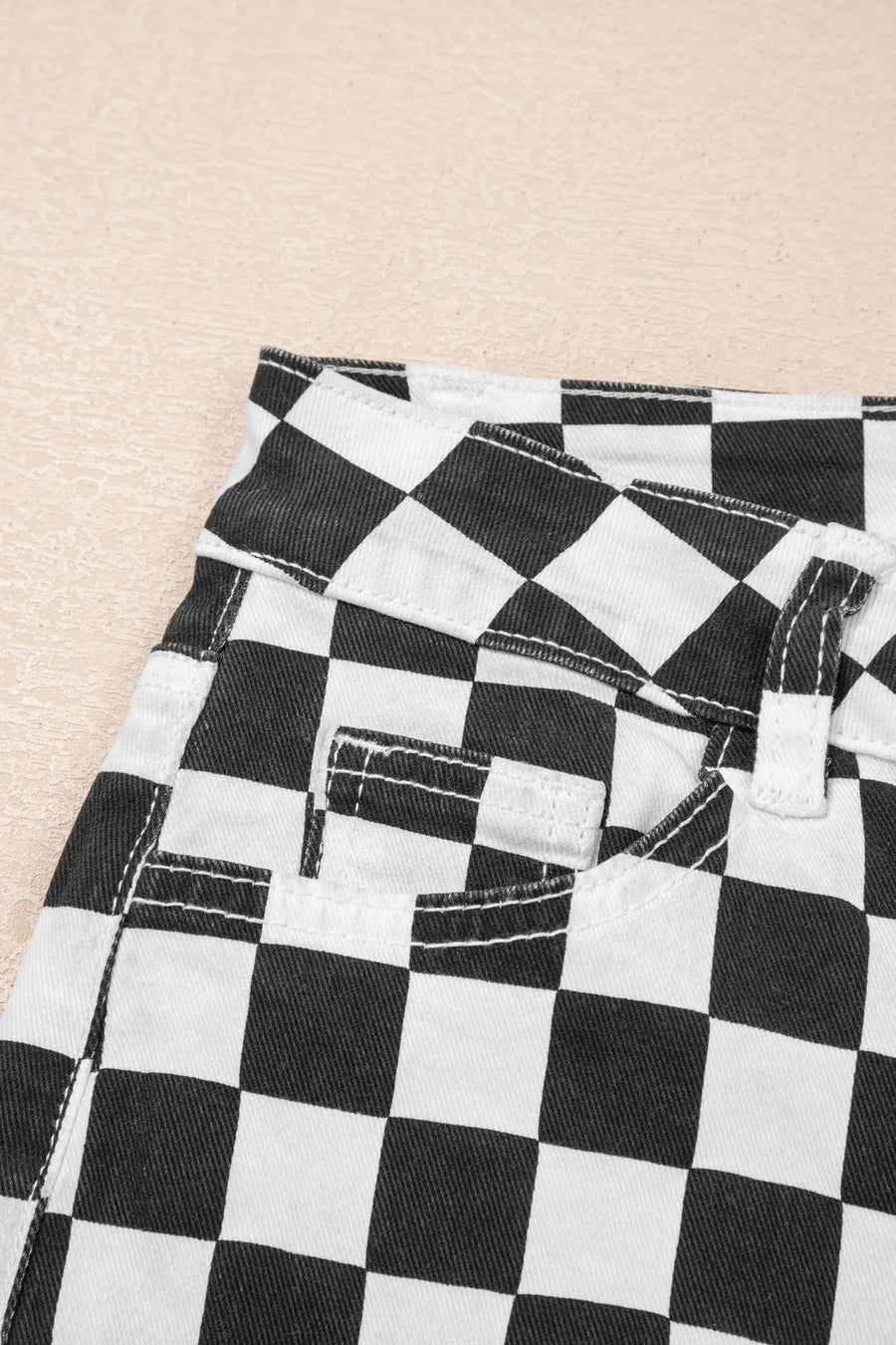 Checkerboard distressed cropped jeans in black and white denim with visible stitching details.
