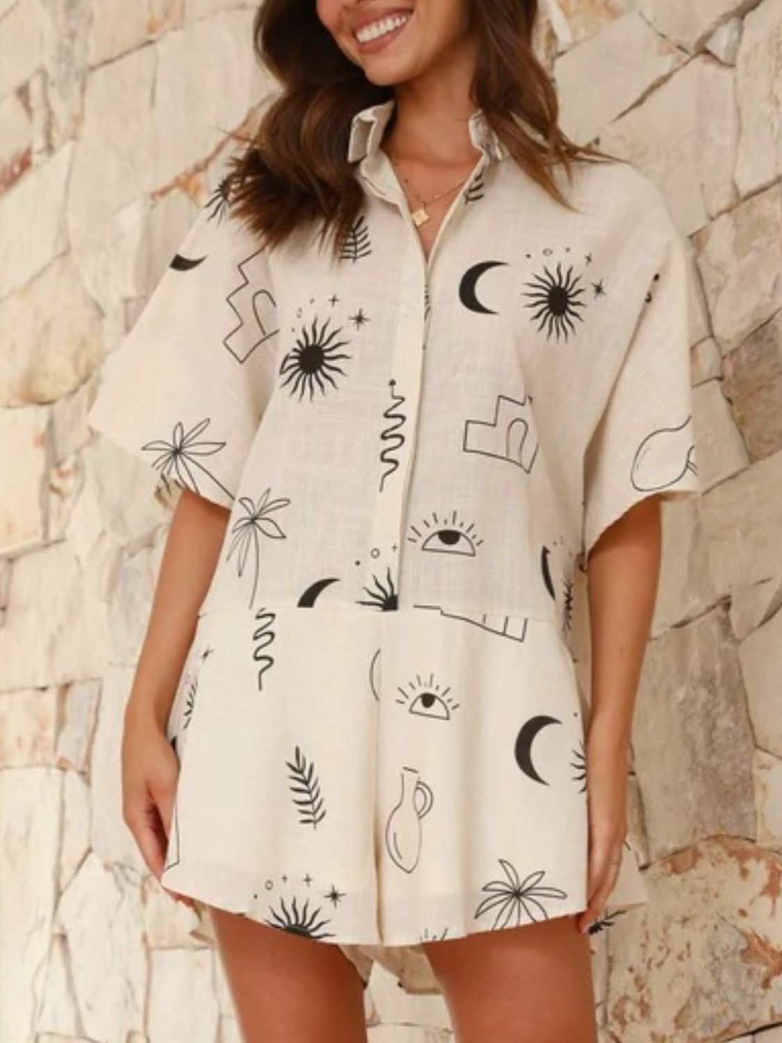 Beige linen romper with celestial print, button front, short sleeves, and flared hem.