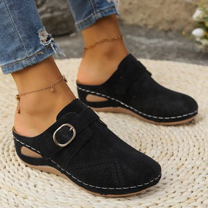 Black laser-cut buckle mule wedges with white stitching and a wedge heel.