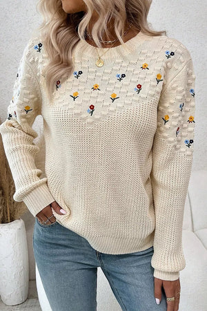 Beige round-neck sweater with embroidered floral pattern and textured sleeves.