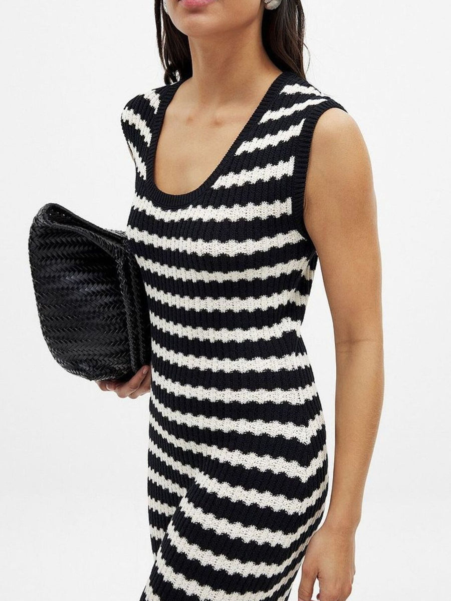 Sleeveless striped knit midi dress with scoop neck and side slit, held with a black clutch.