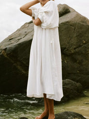 White midi dress with puff sleeves and tie-neck, cinched waist, and flowing skirt.