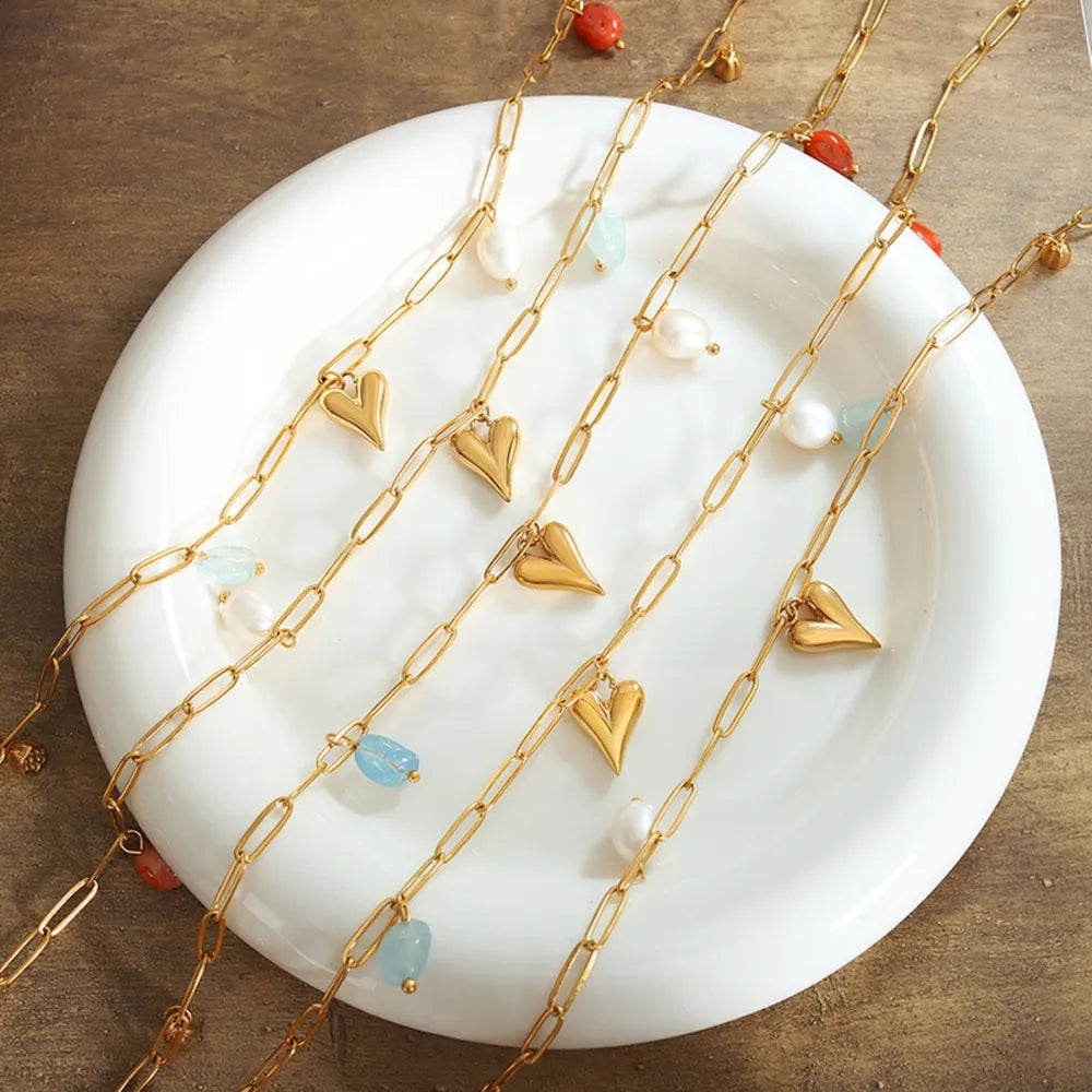 Gold paperclip chain necklace with heart charms, pearls, and blue and red beads.