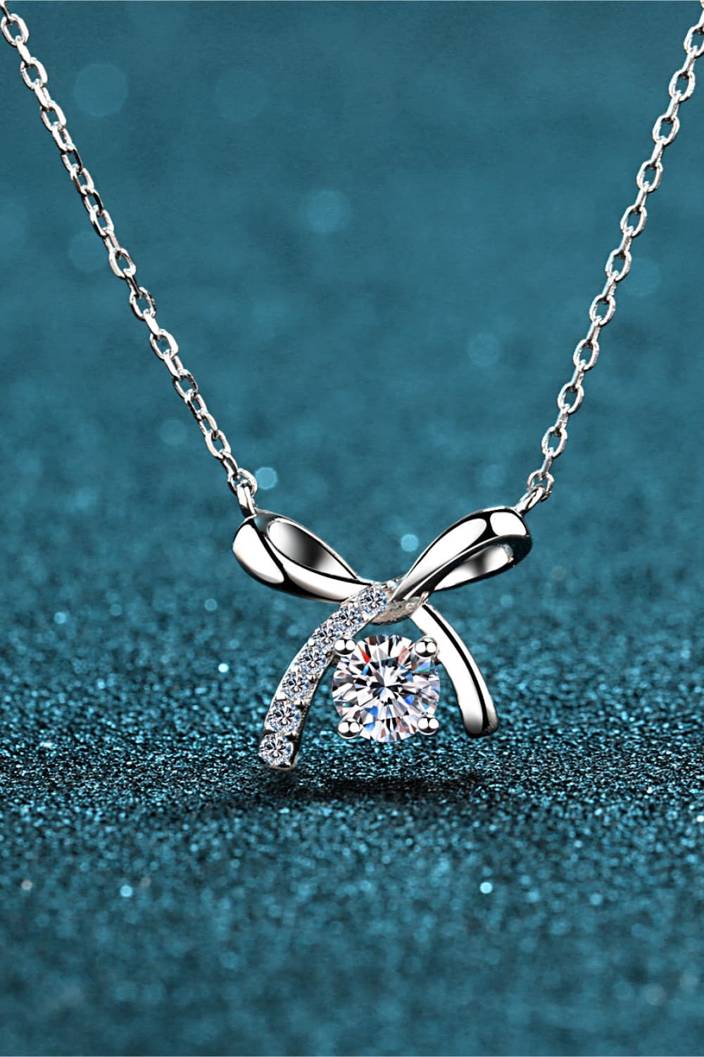Silver bow-tie diamond pendant necklace with a central round-cut diamond and accent stones.