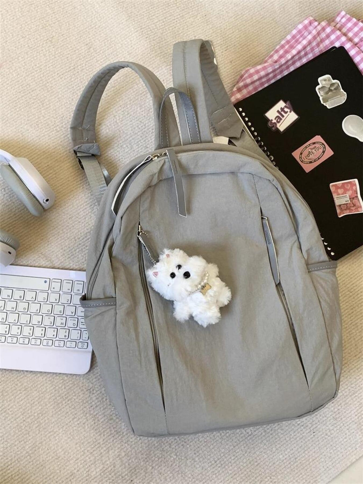 Light gray nylon backpack with fluffy white dog charm and zippered pockets.