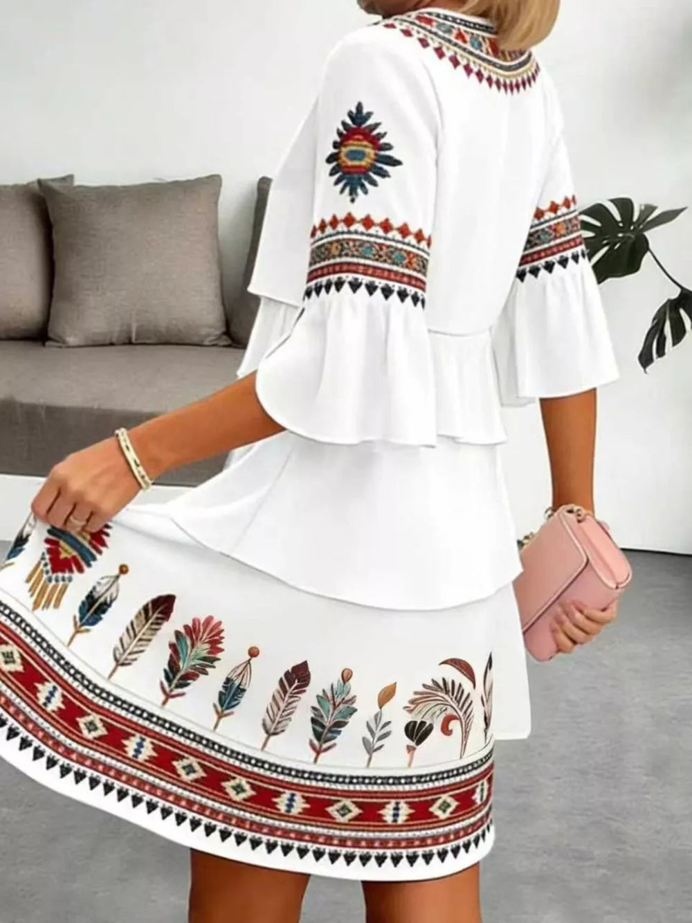 White boho tiered dress with ruffled sleeves and colorful feather print skirt.