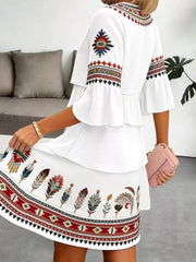 White boho tiered dress with ruffled sleeves and colorful feather print skirt.