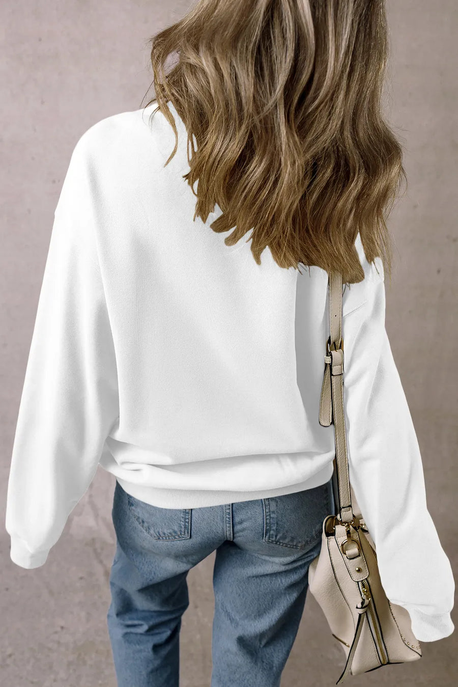 White long-sleeve sweatshirt with a relaxed fit, styled with blue jeans and a crossbody bag.