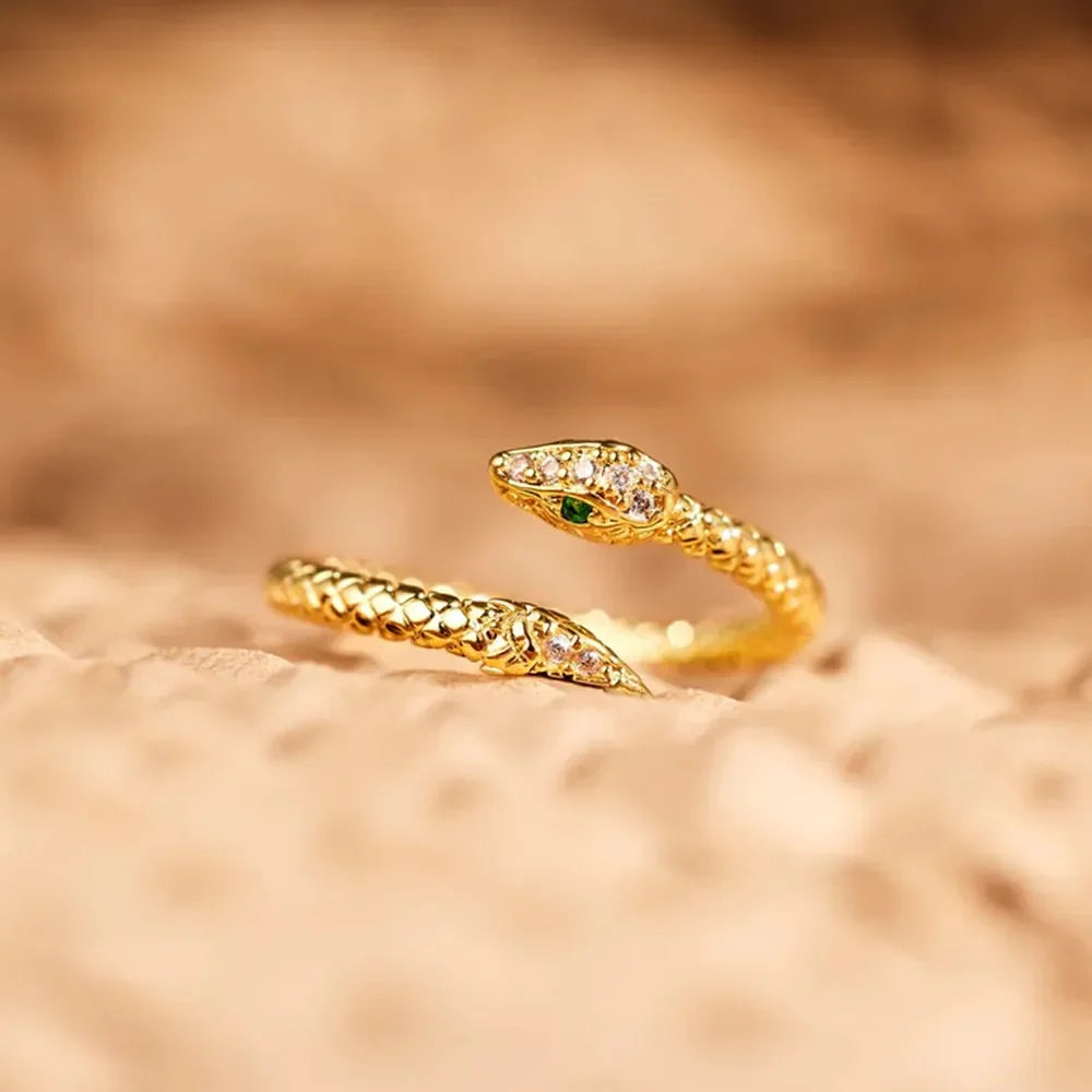 Gold bypass ring with diamond accents and a green eye, shaped like a serpent.