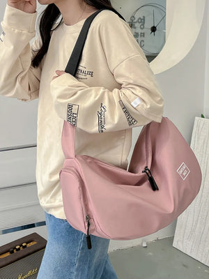 Slouchy crescent crossbody bag in Dusty Pink with adjustable strap and multiple zippered pockets.