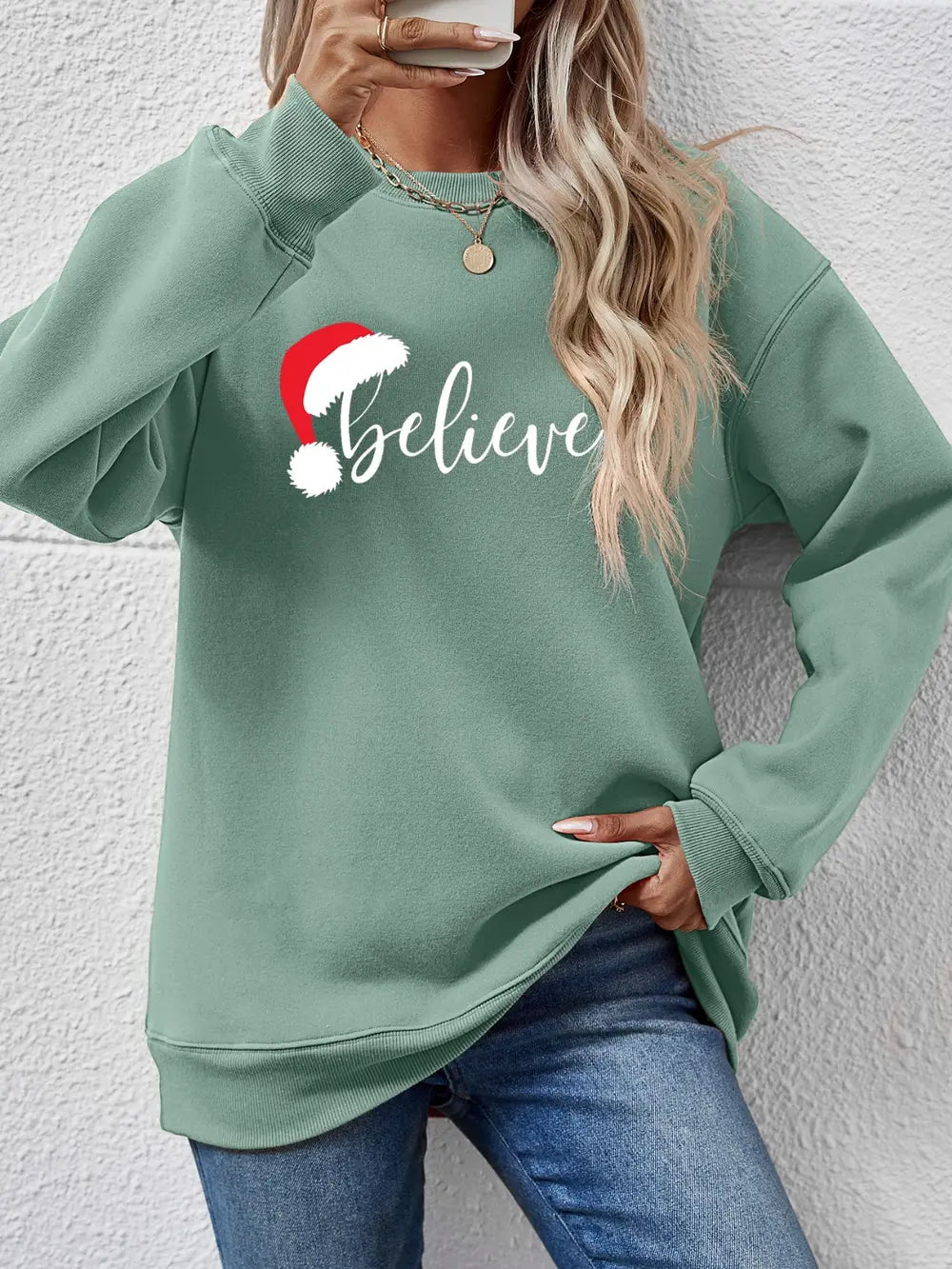 Sage raglan sweatshirt with white "Believe" text and Santa hat graphic.