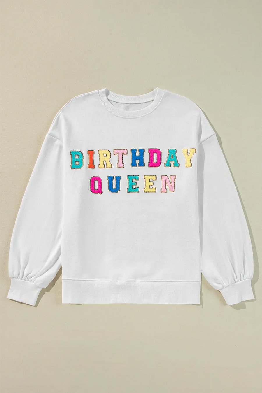 White sweatshirt with puff sleeves and colorful "Birthday Queen" text graphic.