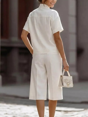 White two-piece set with cropped wide-leg pants and short-sleeve collared shirt, featuring pockets.