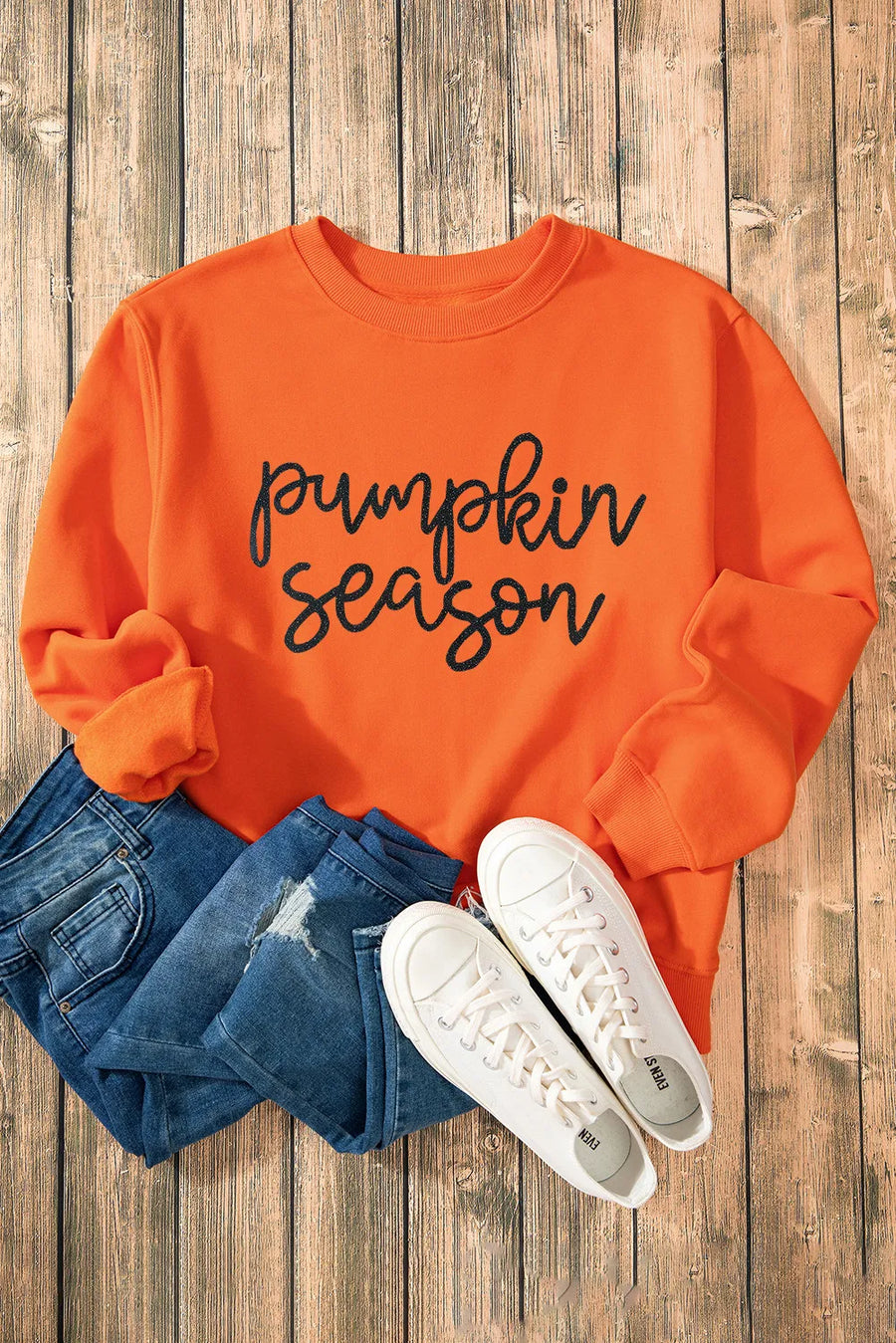 Orange graphic sweatshirt with "pumpkin season" text, cuffed sleeves, paired with jeans and sneakers.